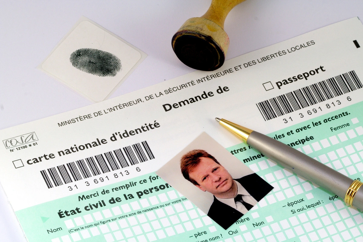 Demande de carte nationale d'identité avec photo d'identité, empreinte digitale et tampon, accompagnée d'un stylo doré sur un formulaire administratif.